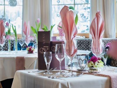 Eleganter gedeckter Tisch mit rosa Servietten und Kerzen neben einem hellen Fenster.