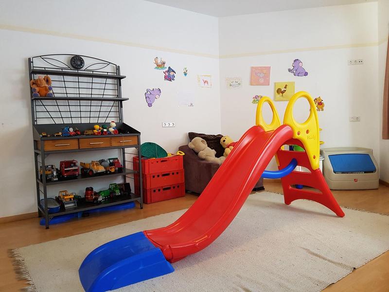 Kinderspielzimmer mit roter Rutsche, Spielzeugregal und Wanddekoration aus Schmetterlingen.