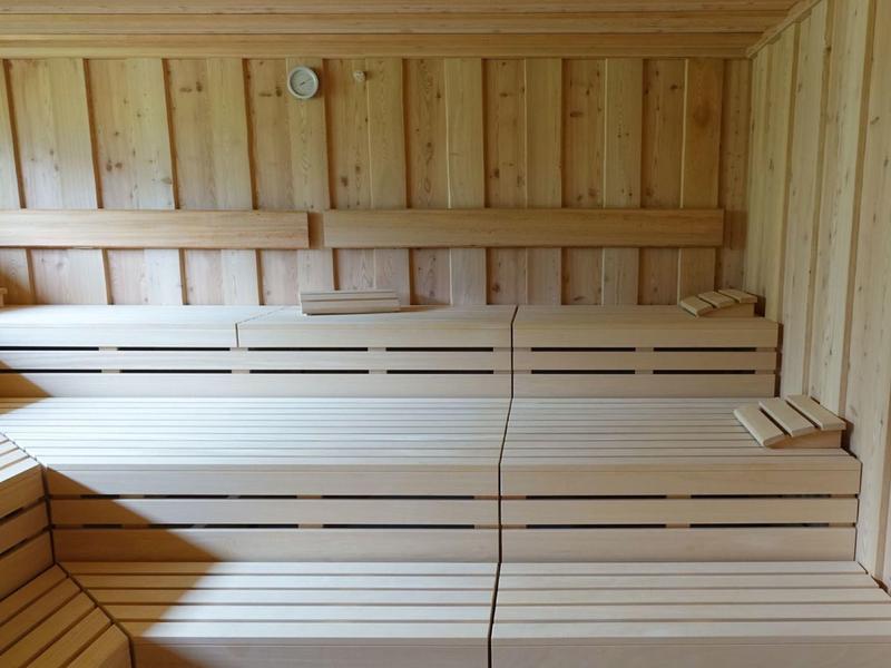 Innensauna mit gestuften Holzsitzbänken aus hellem, glattem Holz und gedämpfter Beleuchtung.