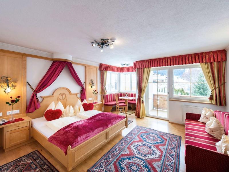 Helles Schlafzimmer mit Holzmöbeln, rotem Bettüberwurf, Teppichen und großem Fenster mit Balkon.