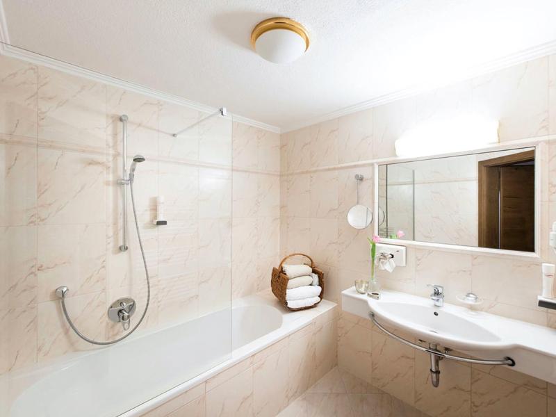 Helles Badezimmer mit beiger Fliesenwanne, Glasbadewannenabtrennung und großem Spiegel über dem Waschbecken.