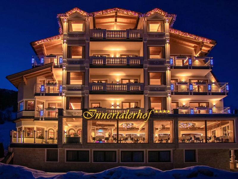 Mehrstöckiges Hotel mit Balkonen, warm beleuchtet bei Nacht, dunkelblauem Himmel im Hintergrund.