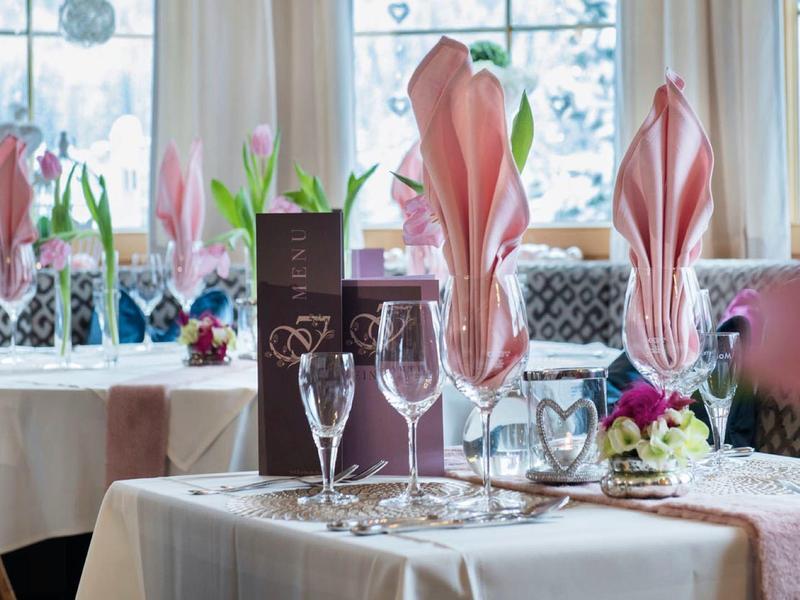 Eleganter gedeckter Tisch mit rosa Servietten und Kerzen neben einem hellen Fenster.