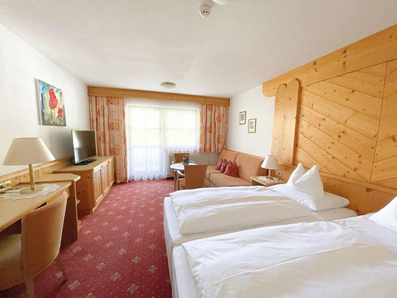 Helles Hotelzimmer mit zwei Betten, rotem Teppich, Holzwand und Fenster mit Vorhängen.