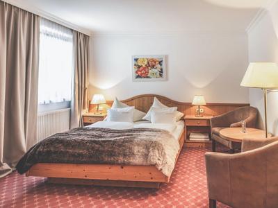 Gemütliches Schlafzimmer mit braunem Teppich, Doppelbett, Nachttischen, Sessel und Beleuchtung.