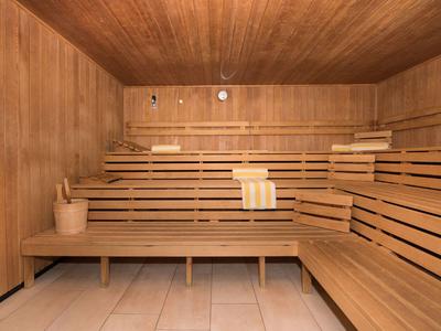 Holzsauna mit mehrstufigen Sitzbänken, Holzverkleidung, Eimer und Kelle, hellem Fliesenboden.