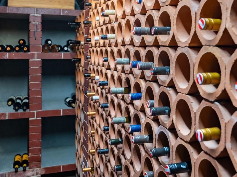 Weinregal aus Terrakotta-Röhren mit verschiedenen Weinflaschen in einem Kellerraum.