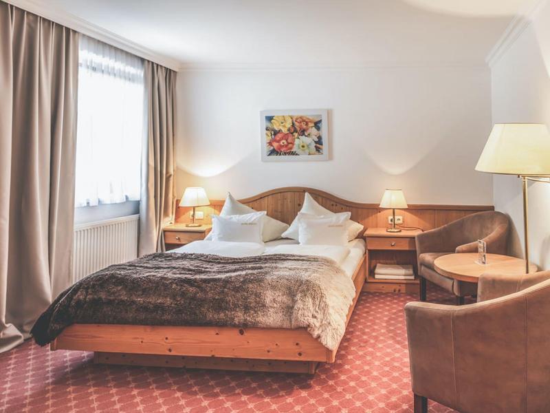 Gemütliches Schlafzimmer mit braunem Teppich, Doppelbett, Nachttischen, Sessel und Beleuchtung.