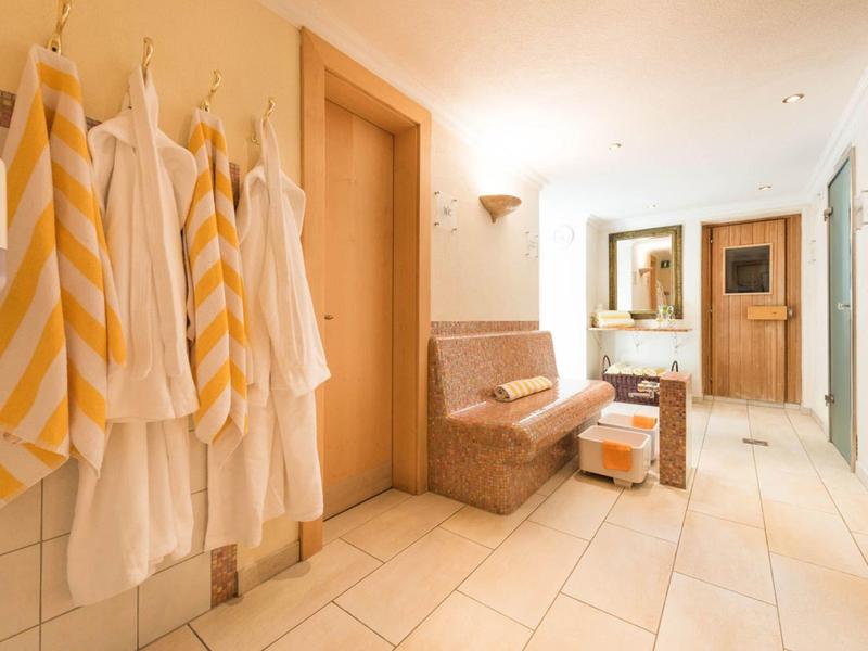 Hell beleuchteter Flur mit weißen Wänden, gelb-weißen Handtüchern und einer Polstersitzbank.