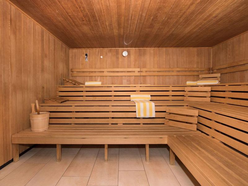 Holzsauna mit mehrstufigen Sitzbänken, Holzverkleidung, Eimer und Kelle, hellem Fliesenboden.