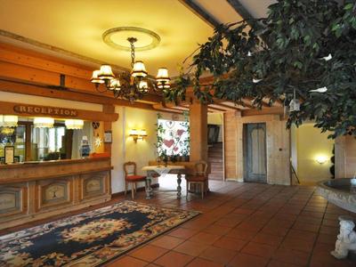 Hotel lobby with reception desk, chairs, carpet, and large plants under warm lighting.