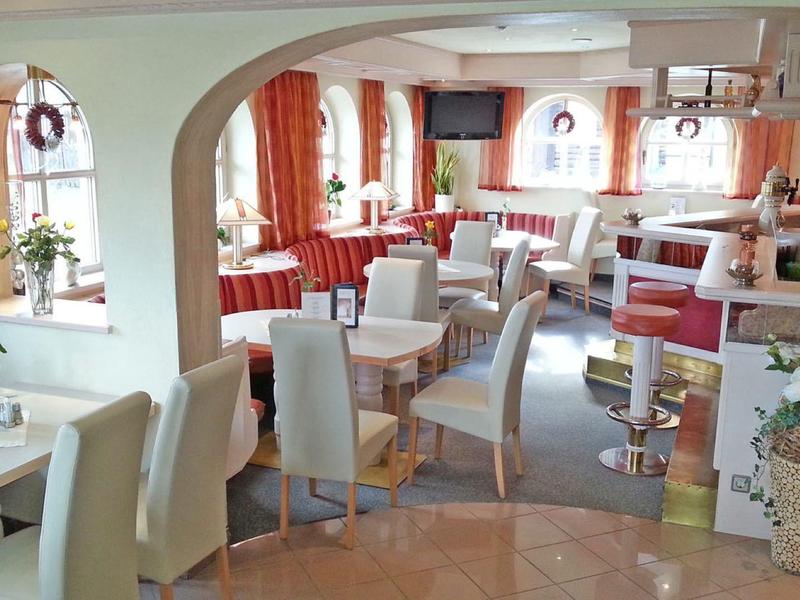 Helles, gemütliches Café mit weißen Stühlen, Holztischen und warmen Orangetönen an den Fenstern.