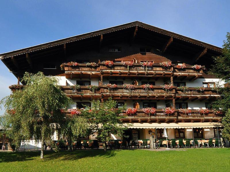Großes Holzhaus im Alpenstil mit Balkonen und roten Blumen vor blauem Himmel.