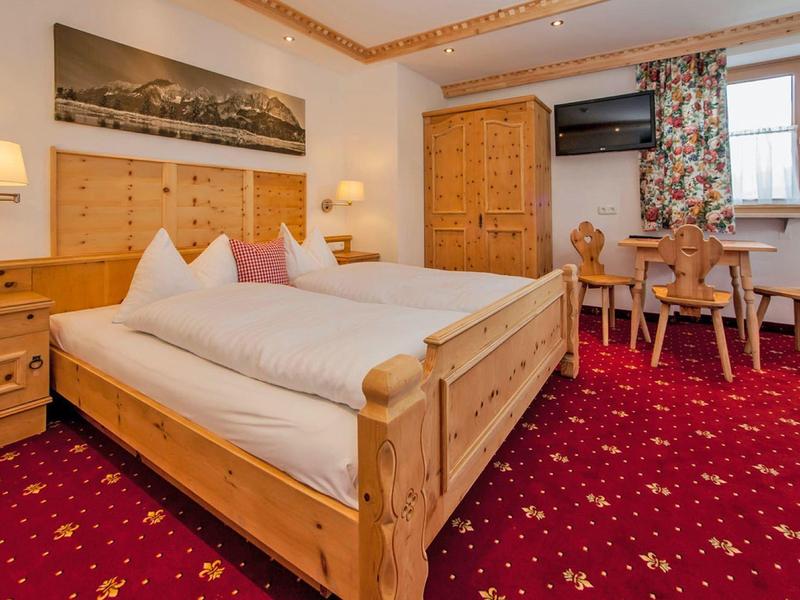 Gemütliches Schlafzimmer mit Holzmöbeln, rotem Teppich, Doppelbett und Fenster mit Vorhängen.