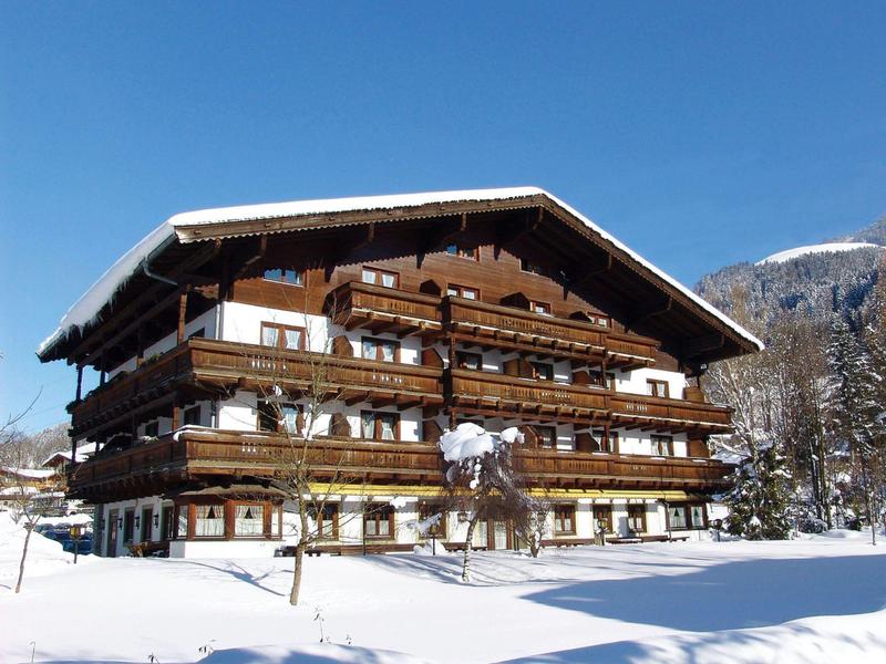 Großes Chalet aus Holz mit mehreren Balkonen, umgeben von Schnee und Bergen im Hintergrund.