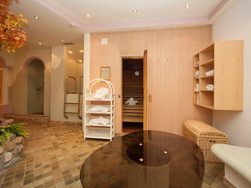 Heller Wellnessraum mit Holzsauna, Steinboden, Pflanzen und runden Tischen aus dunklem Glas.