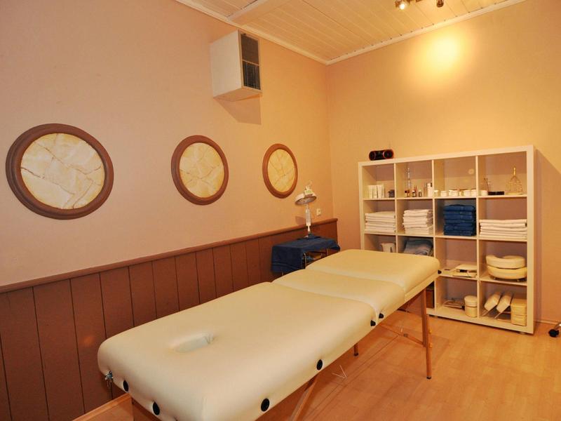 Behandlungsraum mit Massagebank, rundem Wanddekor und Regal mit Handtüchern und Gerätschaften.