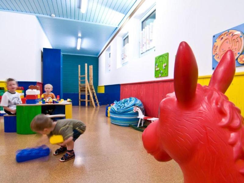Kinderspielraum mit buntem Spielzeug, Möbeln und großem roten Hüpfpferd im Vordergrund.