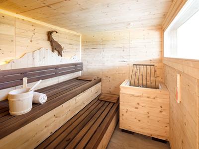 Moderne Holzsauna mit dunklen Holzliegen, hellen Wänden und großem Fenster im Innenbereich.