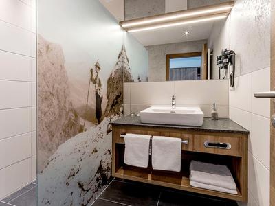 Moderner Badezimmerwaschtisch mit Waschbecken, Holzregal, weißen Handtüchern und großem Wandspiegel.