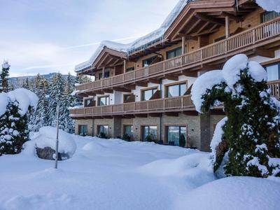 Schneebedecktes Holzhaus mit Balkon vor verschneiter Landschaft und Bäumen im Winter.