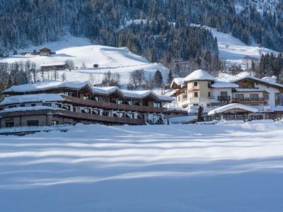 Großes Hotelgebäude im schneebedeckten Tal vor bewaldeten und verschneiten Bergen im Hintergrund.