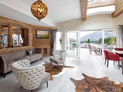 Soggiorno luminoso con poltrone moderne, accenti in legno e vista su terrazza e montagne.