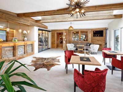 Zona lounge dell'hotel luminosa con poltrone rosse, bancone rustico in legno e ampie finestre.