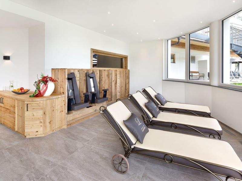 Helle Liegewiese mit weißen Polstersesseln und Holzmöbeln vor großen Fenstern in modernem Raum.