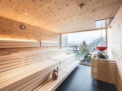 Helle, moderne Sauna aus Holz mit großen Fensterflächen und Panoramablick auf Berge und See.