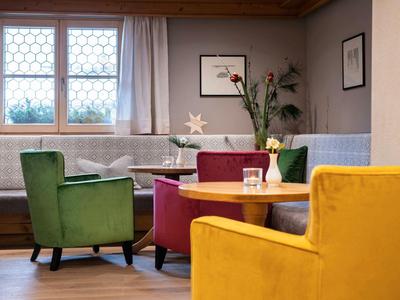 Gemütlicher Sitzbereich mit farbigen Sesseln und einem runden Holztisch in einem Hotelzimmer.