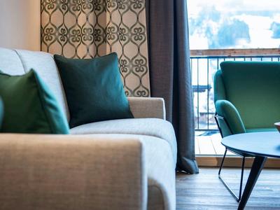 Hellgraues Sofa mit grünen Kissen, runder Tisch mit Obstschale, großer Balkon mit Metallgeländer.