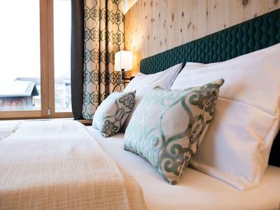 Modernes Schlafzimmer mit großem Bett, weißen Kissen, gemusterten Zierkissen und Tageslichtfenster.