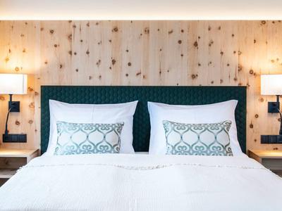 Modernes Schlafzimmer mit großem Bett, weißen Kissen, Holzwand und zwei Wandlampen.