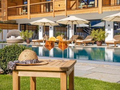 Liegstühle und Sonnenschirme neben einem Pool vor einem Hotel mit Holzbalkonen.