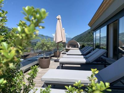 Terrasse mit Liegestühlen und Sonnenschirm mit Bergblick an einem sonnigen Tag.