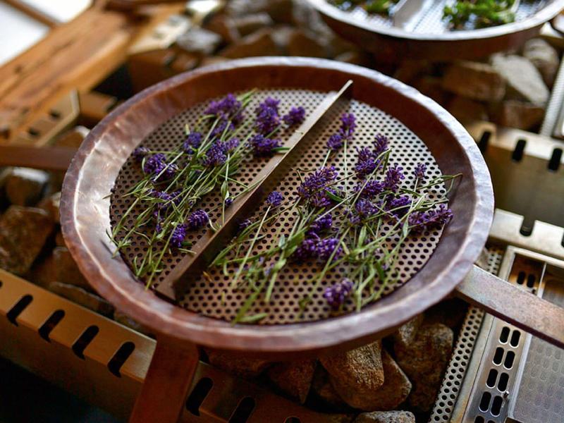 Braune Schale mit Lavendelblüten auf Drahtgitter, liegt auf Holzgestell zum Trocknen.