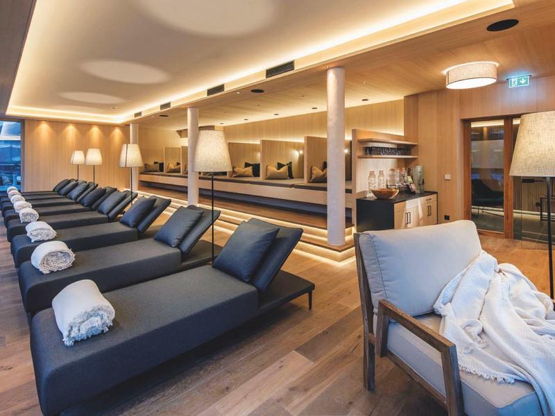 Moderner Spa-Ruheraum mit schwarzen Liegen, weißen Handtüchern und warmem Holzdekor.