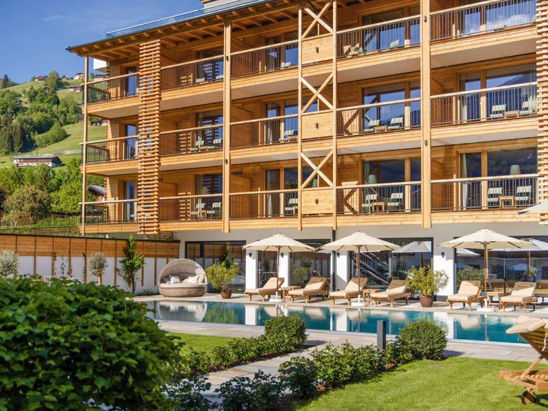 Modernes Holzgebäude mit Terrasse, Sonnenschirmen und Swimmingpool in grüner Gartenanlage.