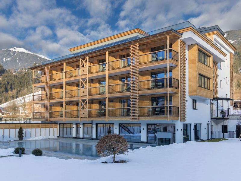 Modernes Holzgebäude mit großen Balkonen, darunter verschneiter Garten und Berglandschaft im Hintergrund.