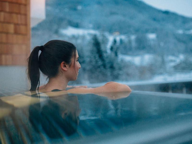 Frau entspannt sich im Pool mit Berglandschaft im Hintergrund, Wasser spiegelt die Umgebung.