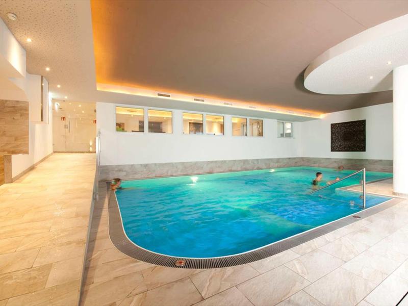 Moderner Hallenpool mit blauem Wasser, großen Fenstern und heller Steinfliesen-Einrichtung.