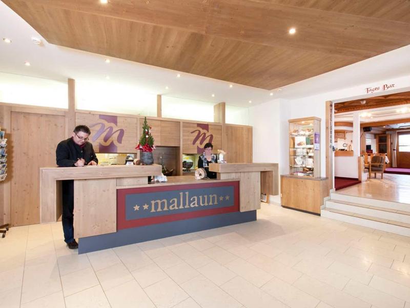 Innenraum einer modernen Rezeption mit zwei Mitarbeitern hinter dem Tresen, hellem Holz und hellen Fliesen.