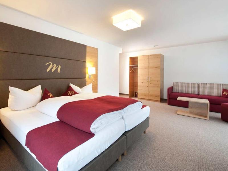 Modern eingerichtetes Hotelzimmer mit Doppelbett, Sofa, Schrank und hellem Teppichboden.