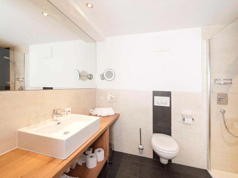 Helles Badezimmer mit weißem Waschbecken, Holzablage, Toilette und Dusche, minimalistisch gestaltet.