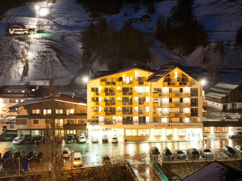Ein hell beleuchtetes Hotel in den Bergen bei Nacht mit schneebedecktem Hang im Hintergrund.