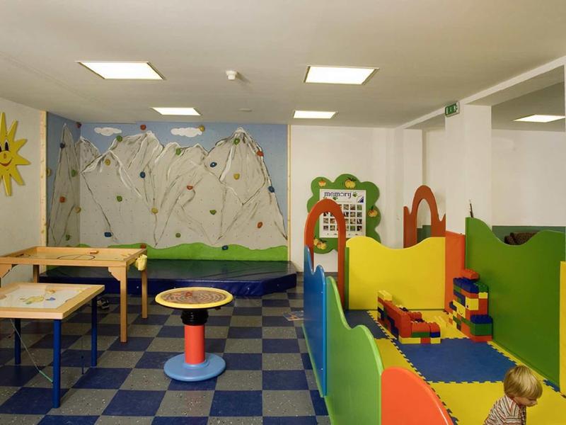 Bunter Spielzimmer mit weichen Matten, kleinen Tischen und Kletterwand in hellem Raum.