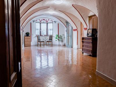 Heller Raum mit gewölbter Decke, braunem Boden und zwei Stühlen vor Fenster mit Gardinen.