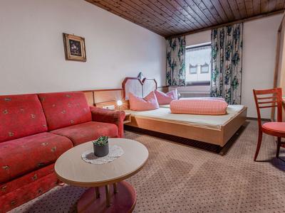 Camera d'hotel accogliente con divano rosso, letto matrimoniale, mobili in legno e moquette.