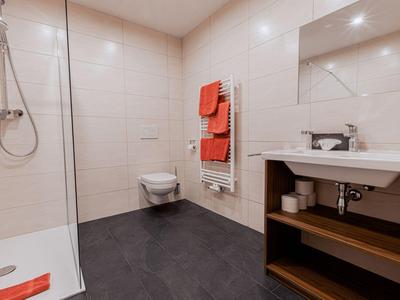 Bagno moderno con doccia, WC, lavabo e asciugamani arancioni.